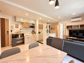 A modern kitchen with built-in appliances, a dining area with a marble table, and a living area with a large TV.