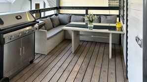 A compact outdoor kitchen area with a grill, a wicker sofa, and a small table with a vase of flowers. - Stunning home in Jaromierz with sauna (Jaromierz)