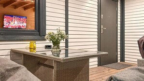 A modern outdoor seating area with a glass-top table, wicker furniture, and a TV screen displaying a sports event. - Stunning home in Jaromierz with sauna (Jaromierz)