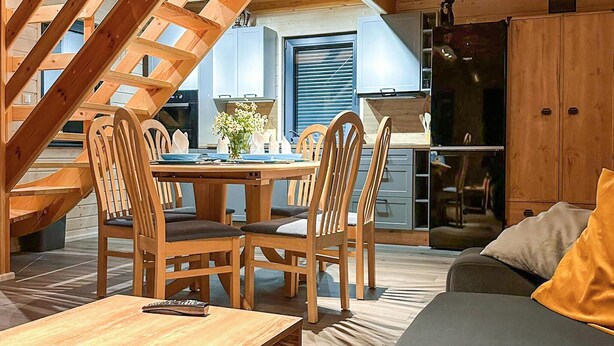 A cozy wooden interior with a dining table set for four, surrounded by wooden chairs. A sofa and a small table with a remote control are visible. - Stunning home in Jaromierz with sauna (Jaromierz)