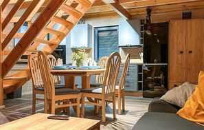 Un interior de madera acogedor con una mesa de comedor dispuesta para cuatro personas, rodeada de sillas de madera. Se ve un sofá y una mesita con un control remoto.