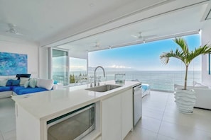 A modern kitchen with a large island, a dining area, and a view of the ocean.