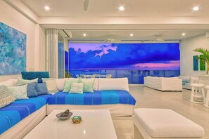 A modern living room with a large sofa, a coffee table, and a view of the sky through a glass wall.