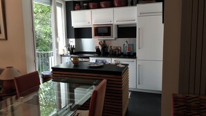 Une cuisine moderne avec une table à manger en verre, des meubles blancs et un plan de travail noir.