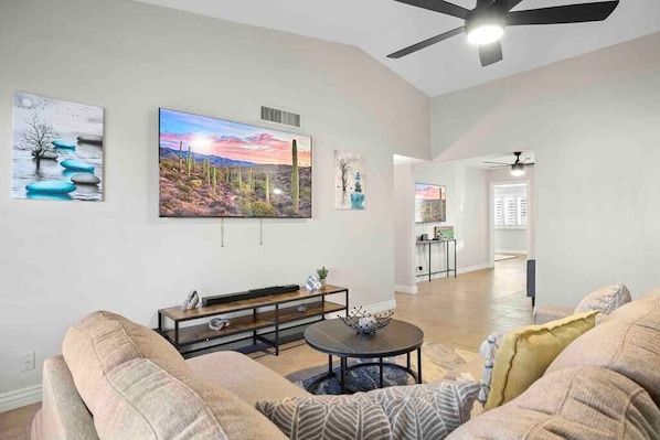 A spacious living room with a large TV, a ceiling fan, and a dining area in the background. - Sahuaro Villa with Pool + Great Location (Scottsdale)