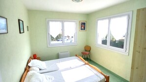 Une chambre avec un lit simple, un cadre en bois, un radiateur, une chaise et deux fenêtres.