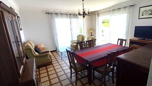 Un espace repas comprenant une table et des chaises, un canapé, un téléviseur et un lustre.