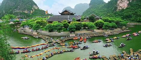 A traditional wooden boat festival with numerous boats on a river, surrounded by lush greenery and traditional buildings.