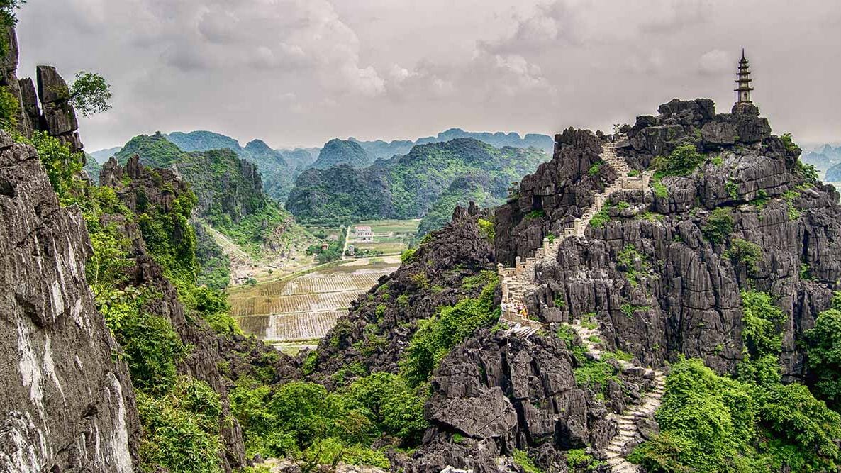 A mountainous landscape with a temple on a cliff, a winding path, and a valley below.