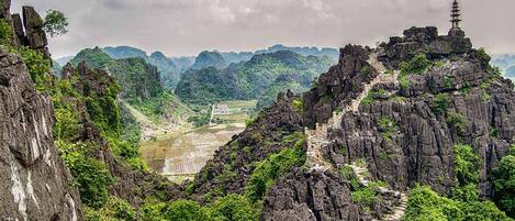 A mountainous landscape with a temple on a cliff, a winding path, and a valley below.