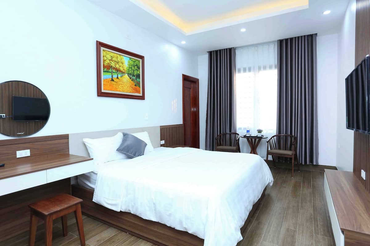 A hotel room with a bed, a desk, a chair, a TV, and a painting on the wall.