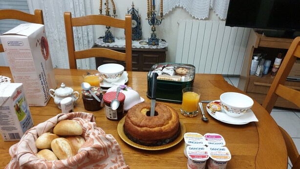 Une table de petit-déjeuner avec du pain, un gâteau, du jus et des pots de yaourt Danone.
