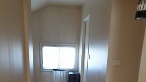 Un couloir étroit avec un plancher en bois, un radiateur, une fenêtre et une valise.