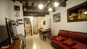 A cozy living room with a red leather sofa, wooden dining table, and a staircase leading to another level. - House of the Olive Grove (Narni Sotterranea with free parking) (Narni Scalo)