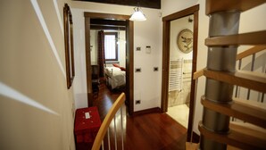 A hallway with a wooden staircase, a bed, a red table, and a wall clock. - House of the Olive Grove (Narni Sotterranea with free parking) (Narni Scalo)