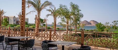 An outdoor seating area with tables and chairs, overlooking a body of water and mountains.