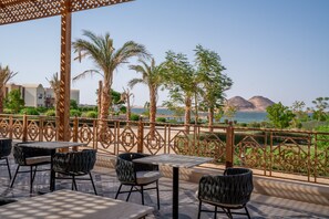 An outdoor seating area with tables and chairs, overlooking a body of water and mountains. - Azal Lagoons Resort Abu Simbel (Abu Simbel)