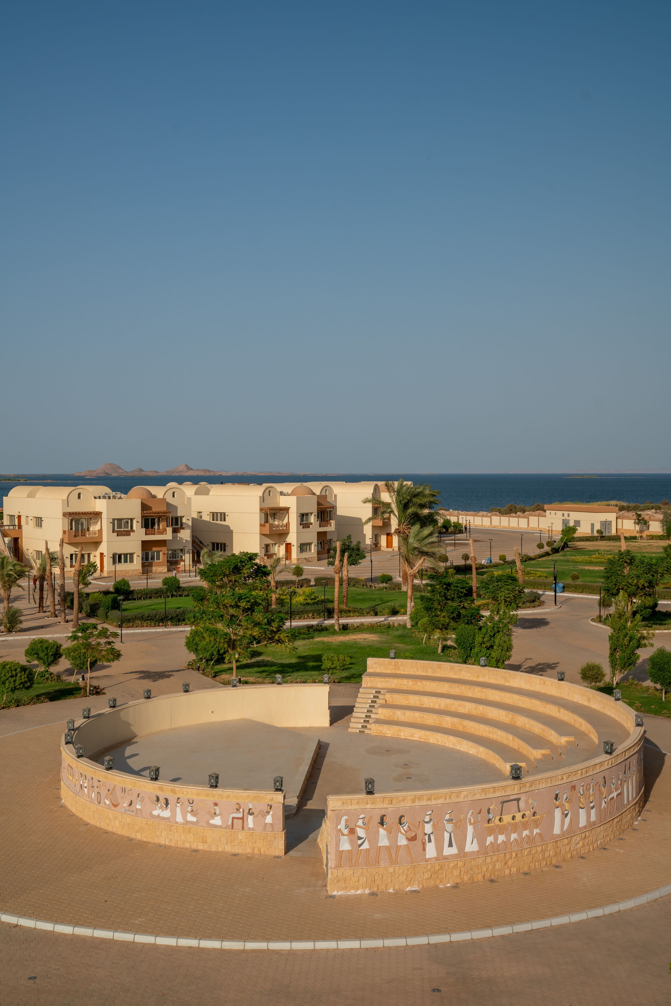 A resort with a central amphitheater, multiple-story buildings, and a view of the sea.