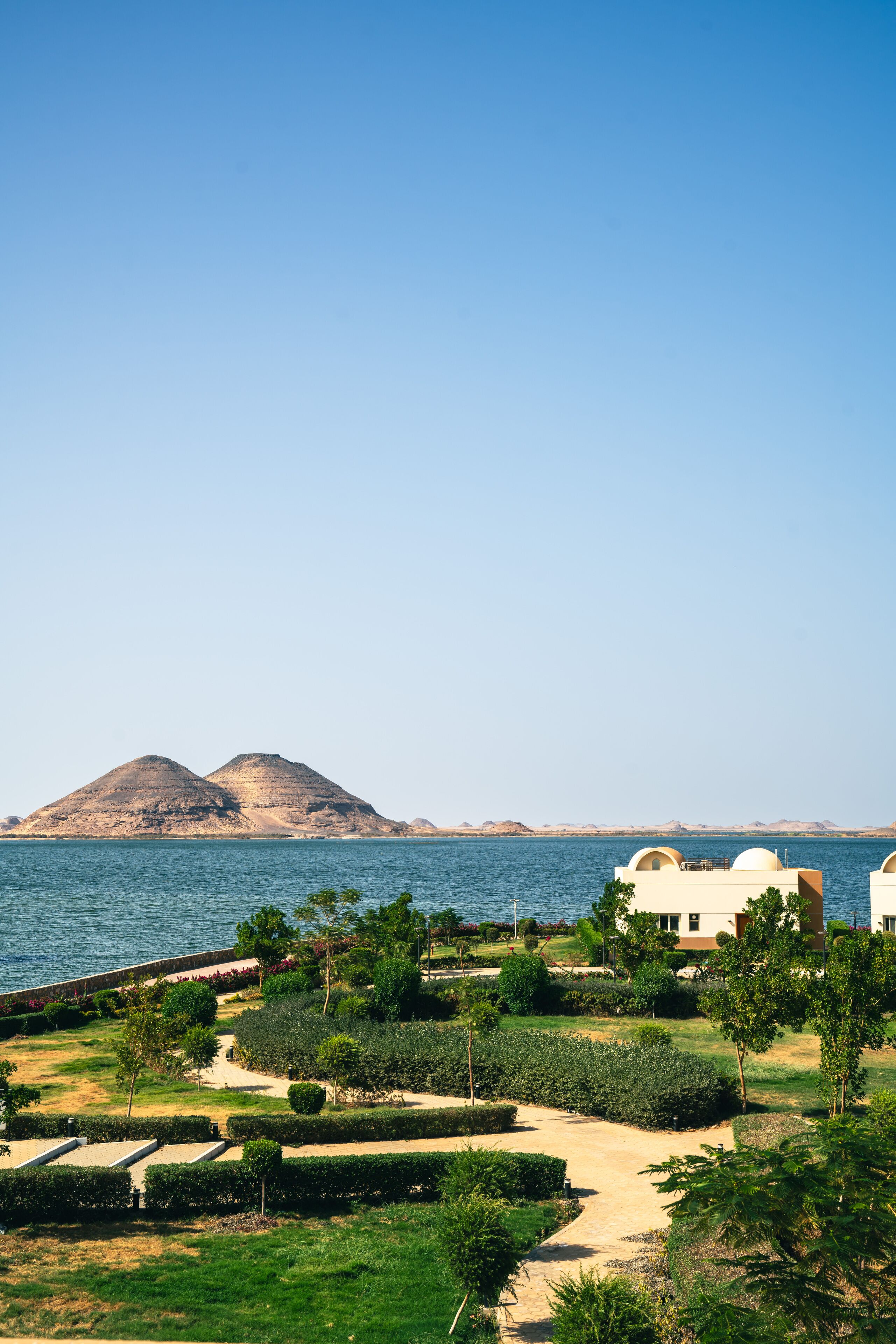 A resort with a clear view of the sea, a landscaped garden, and a mountain in the background.