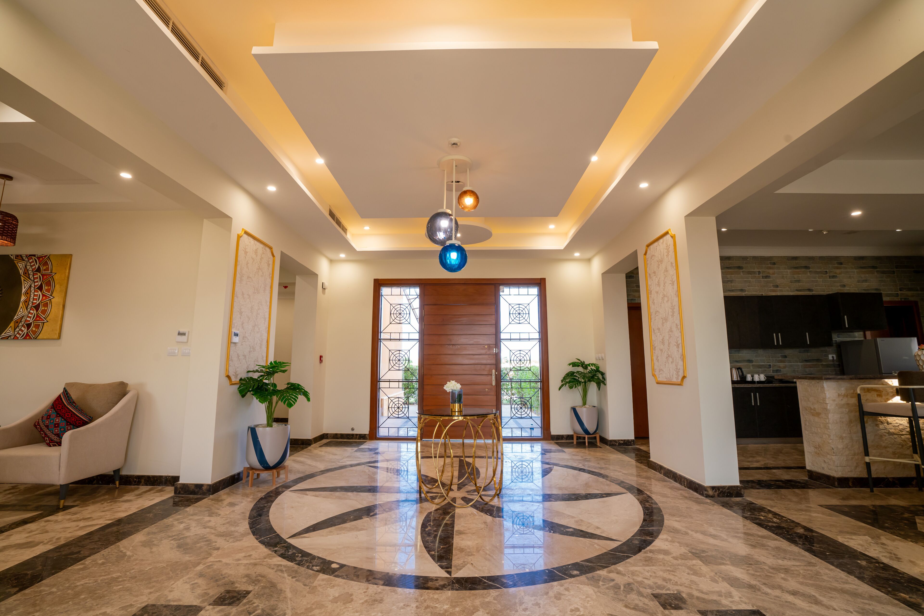 A spacious lobby with a marble floor, a central table, and potted plants.