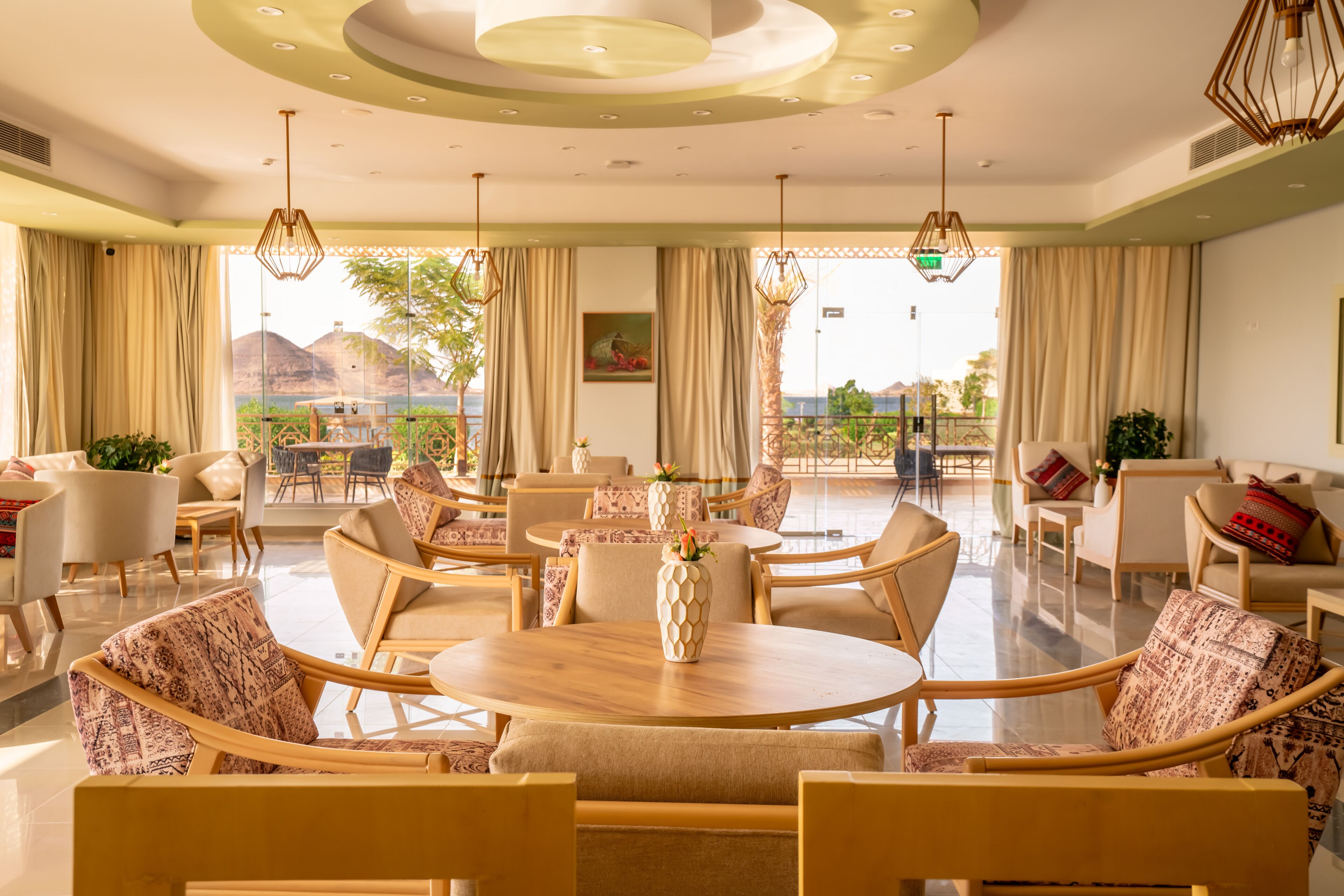 A spacious hotel lobby with a round wooden table, comfortable seating, and a view of the outdoors.