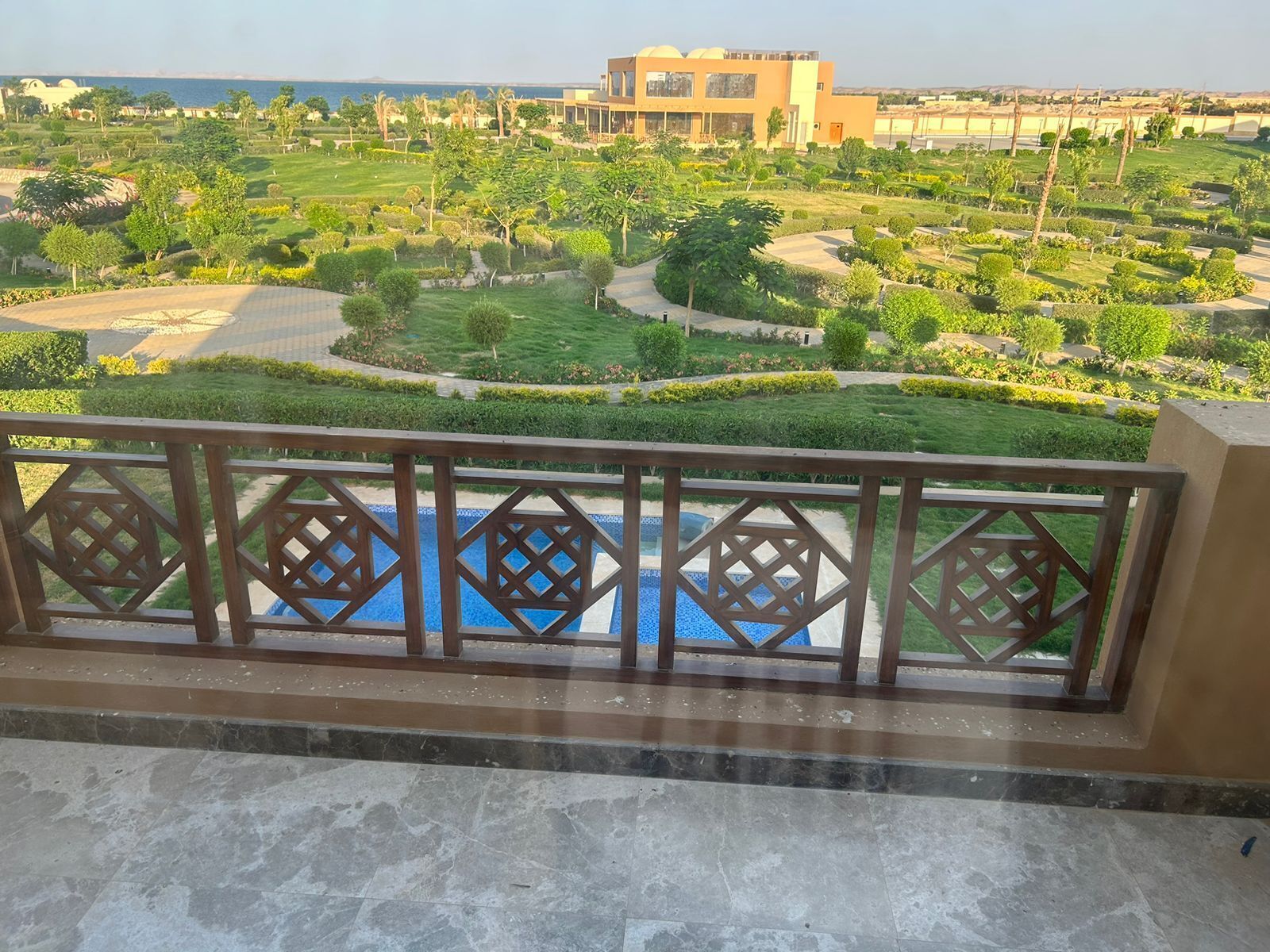 Une vue depuis un balcon donnant sur une piscine, un jardin aménagé et un bâtiment en arrière-plan.