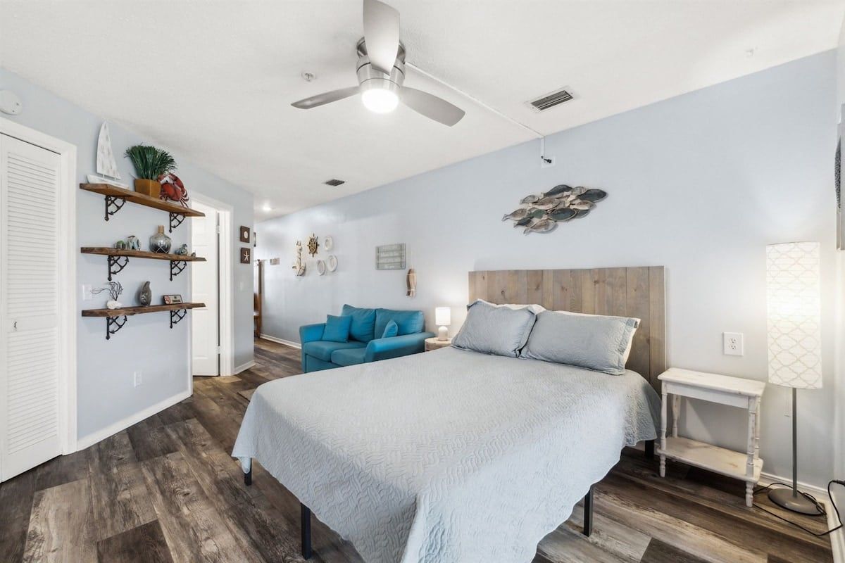 A bedroom with a bed, a ceiling fan, a nightstand, a lamp, and a blue chair.