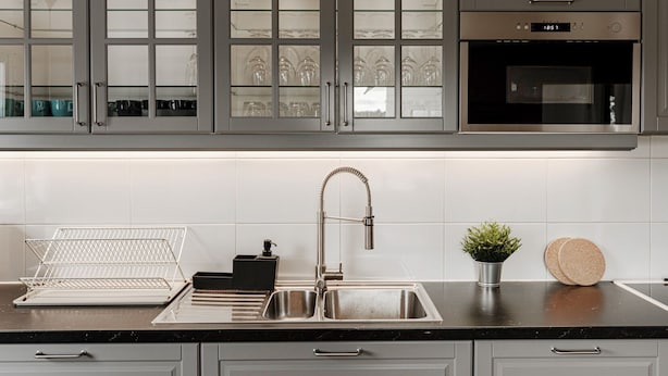 A modern kitchen with grey cabinets, a stainless steel sink, and a built-in oven.