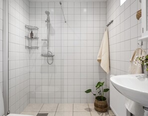 A modern bathroom with white tiles, a shower, a sink, and a potted plant. - Solglimt (Oedsmal)