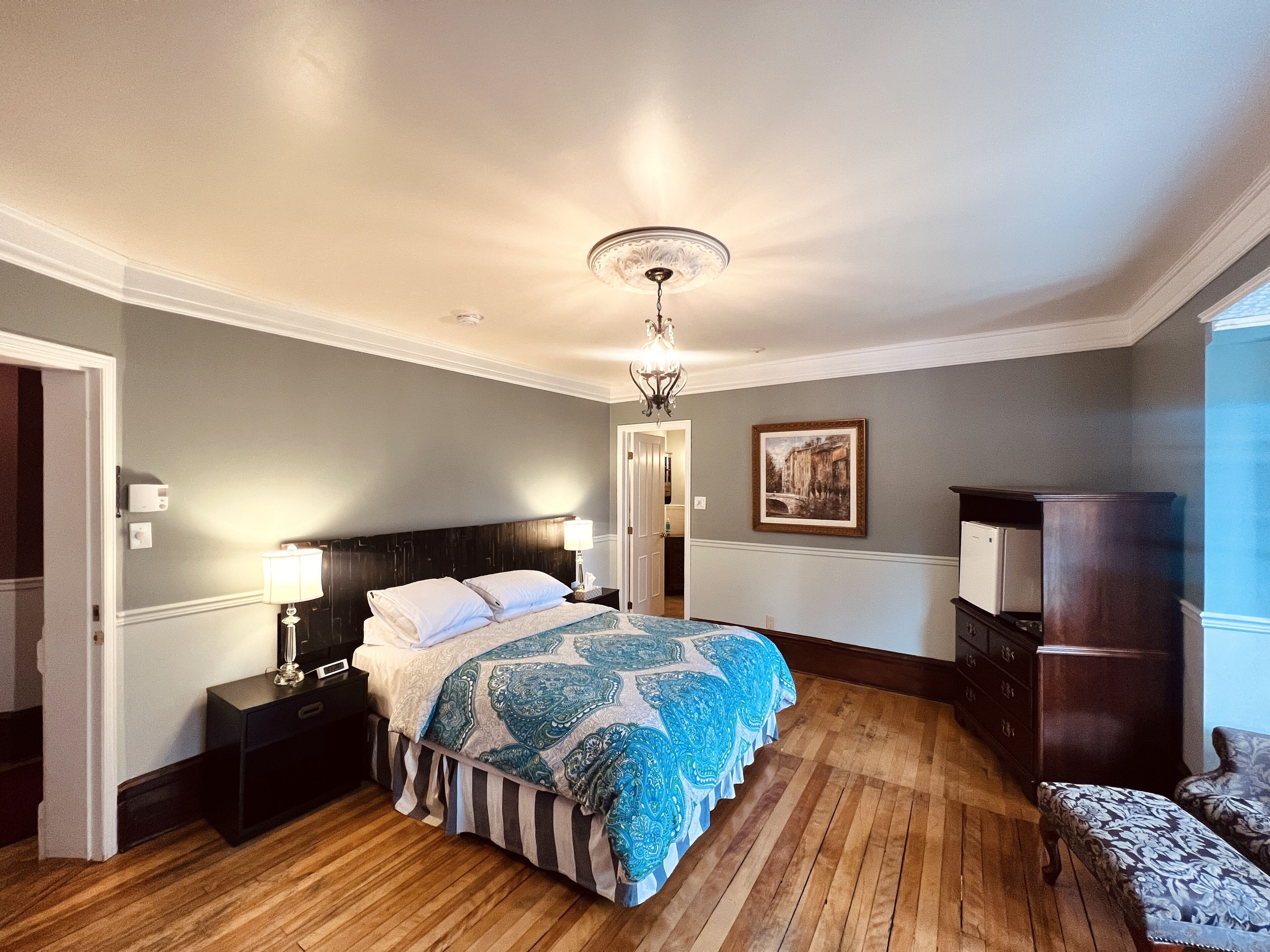 A bedroom with a large bed, a nightstand, a dresser, a chair, and a ceiling light.