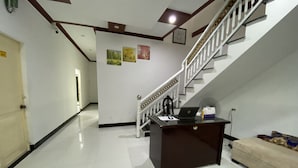A reception desk with a laptop, a telephone, and a small table with a bottle and a tissue box. A staircase with a white railing leads to an upper floor. - Ninh Chu House (Ninh Chu)
