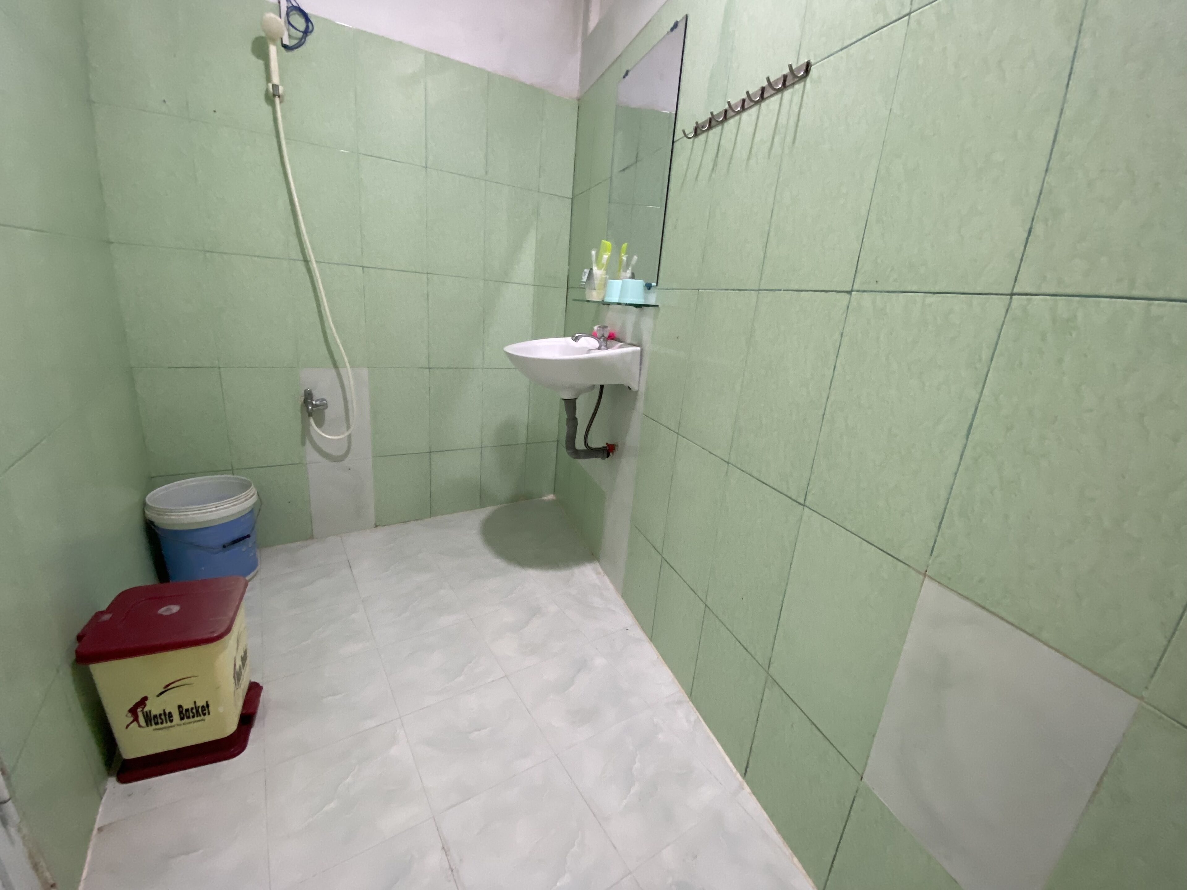 A bathroom with green tiles, a white sink, a mirror, and a waste basket.