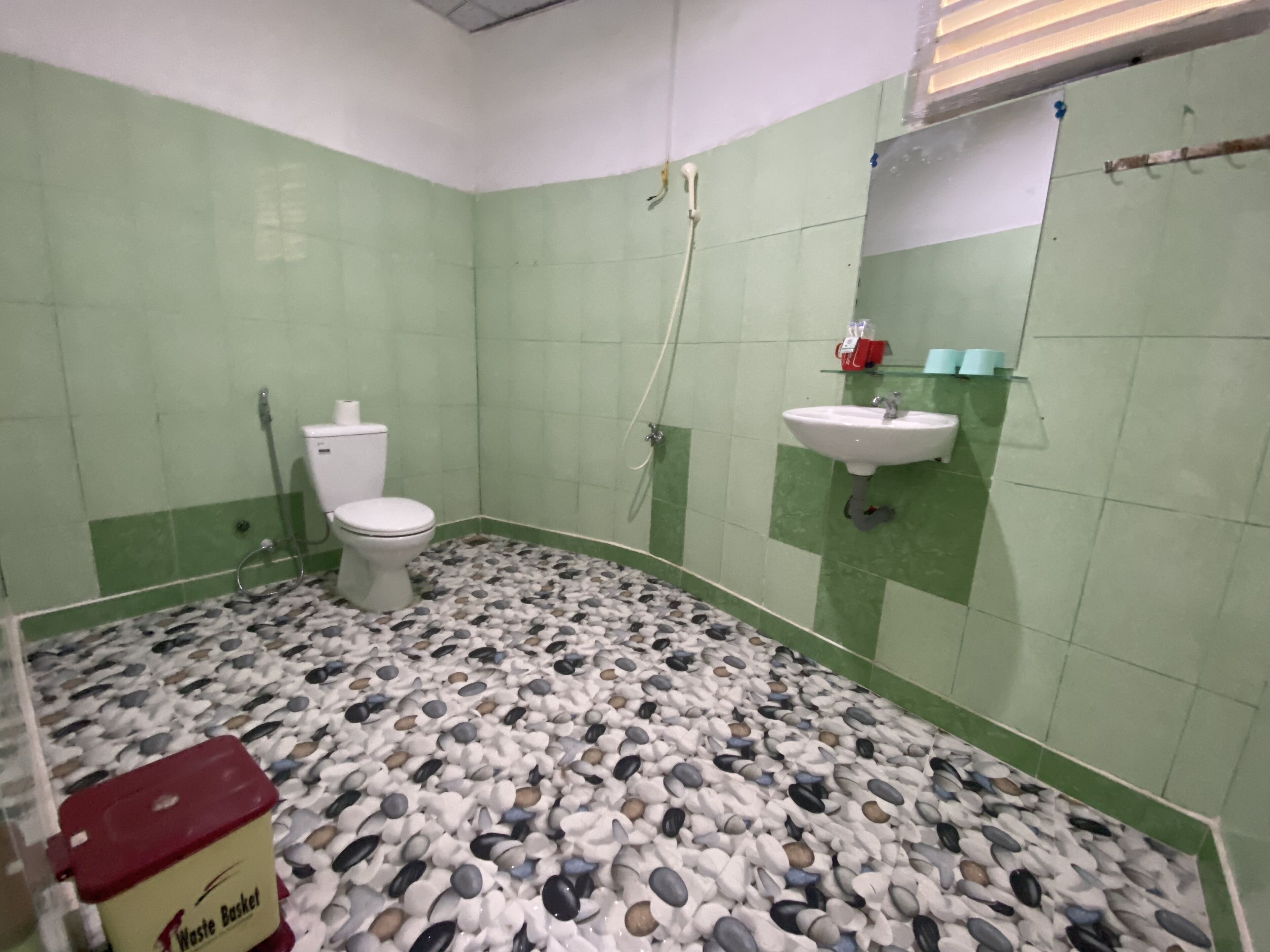 Un baño con inodoro, lavamanos y paredes con azulejos verdes.