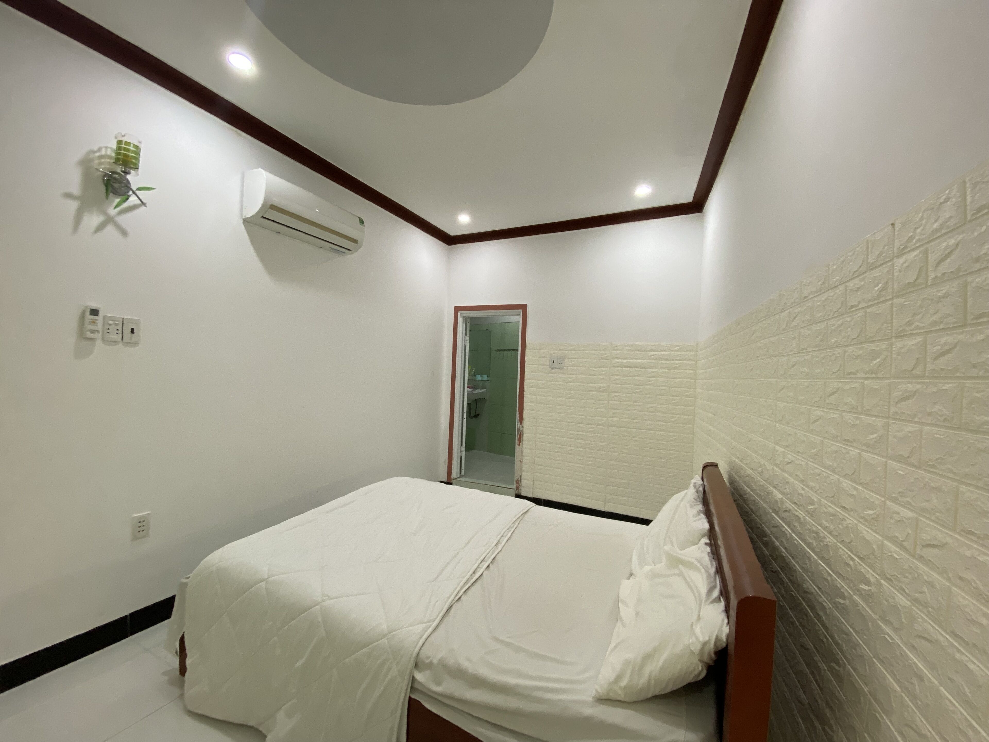 Un dormitorio con cama, aire acondicionado, una lámpara de pared y una puerta que da al baño.