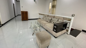 A spacious living room with a sofa, ottoman, glass coffee table, and a cabinet. - Ninh Chu House (Ninh Chu)