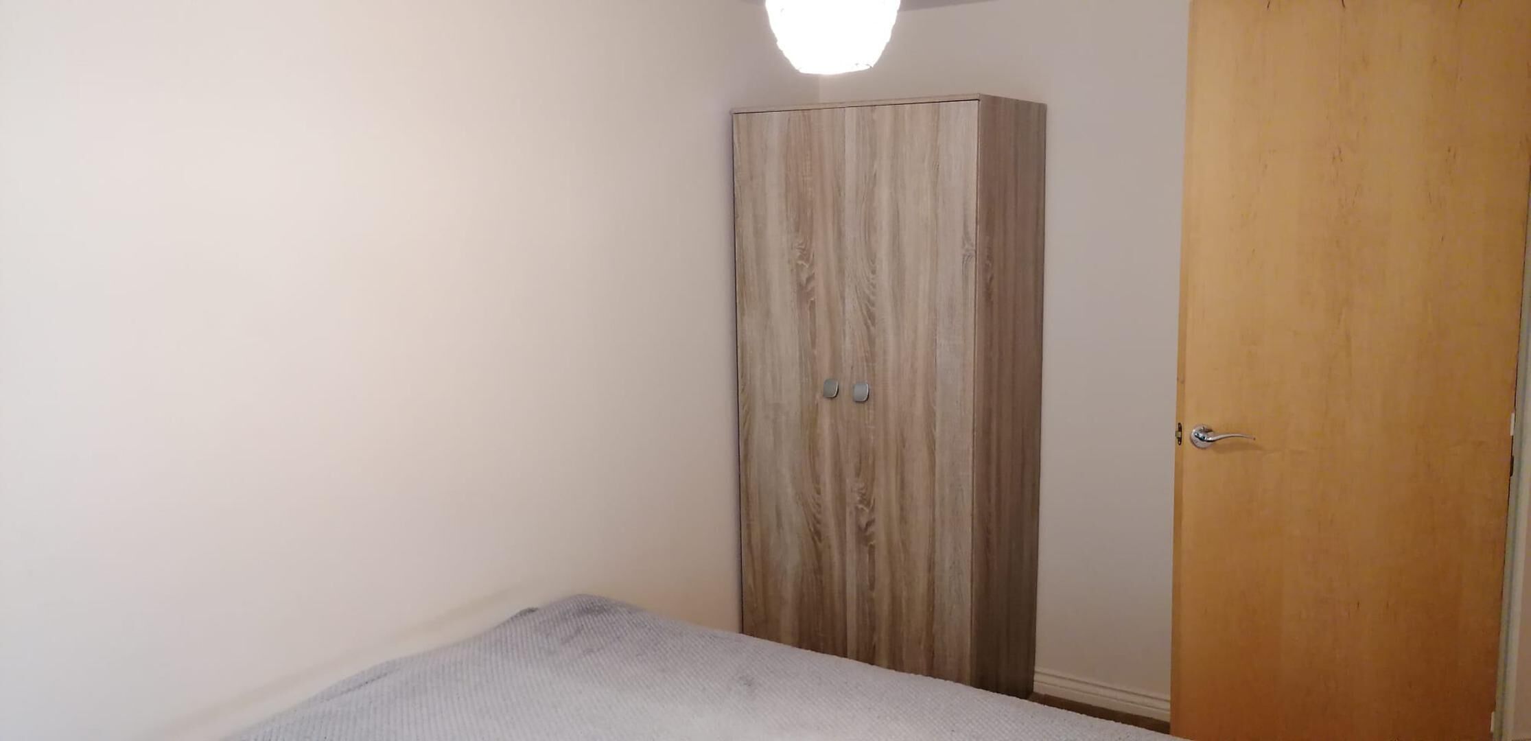 A bedroom with a single bed, a wardrobe, and a door.