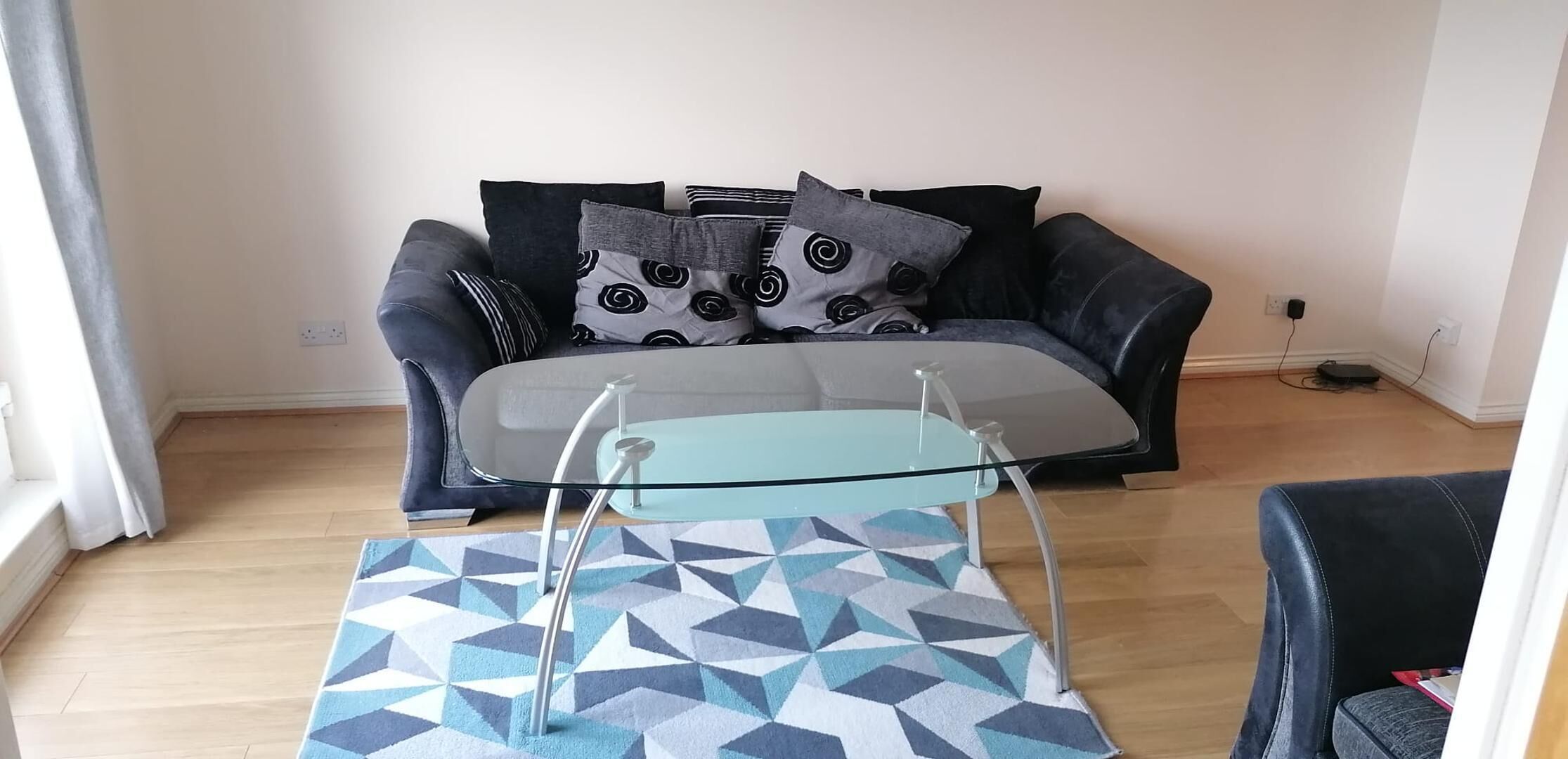 A living room with a sofa, a glass coffee table, and a patterned rug.