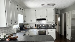 Una cocina moderna con armarios blancos, encimera negra y horno empotrado. Hay dos taburetes en la isla y un fregadero con grifo.