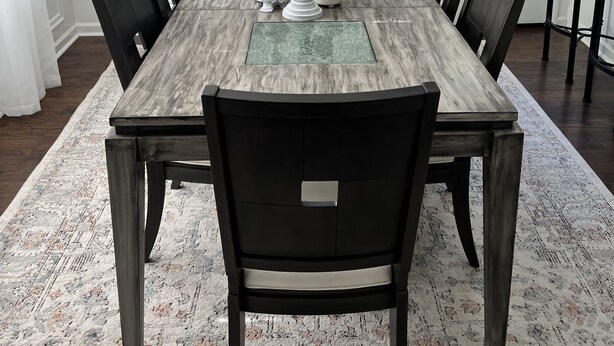 Comedor con mesa de madera, sillas negras, una araña y un cuadro de pájaros en una rama.