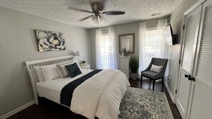 Un dormitorio con cama, ventilador de techo, una silla, cómoda y espejo.