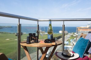 Ein Balkon mit Tisch, auf dem eine Weinflasche, Gläser, Fernglas und ein Buch stehen.