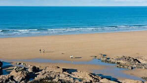 Ampia spiaggia sabbiosa con affioramenti rocciosi in primo piano e un mare calmo.