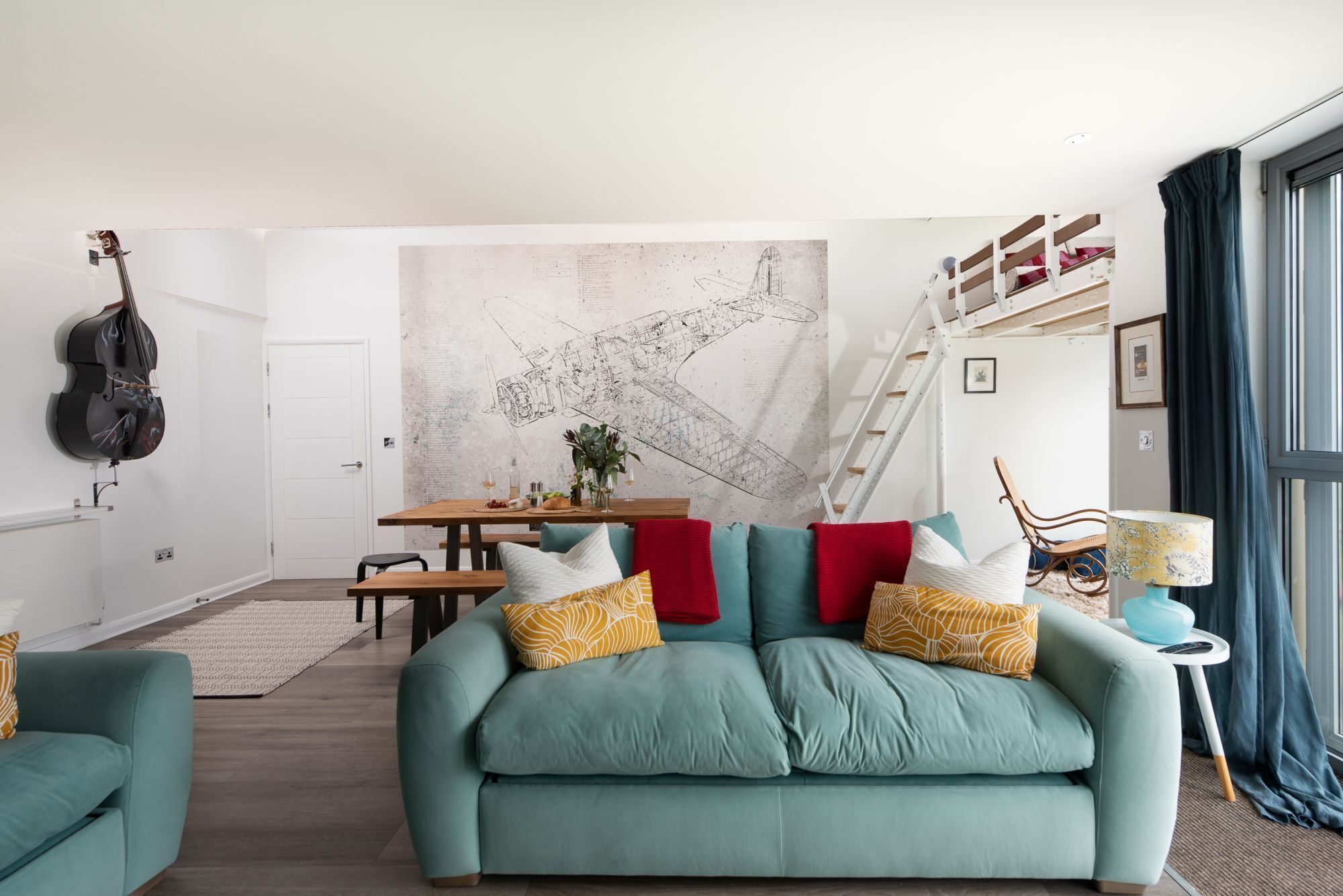 Ein Wohnzimmer mit einem türkisfarbenen Sofa, einem Holzesstisch und einem großen abstrakten Wandbild.