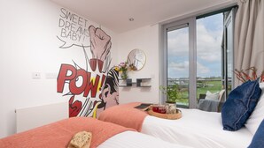 Una camera da letto moderna con due letti, un'ampia finestra vista città e una parete decorata con motivi pop art.