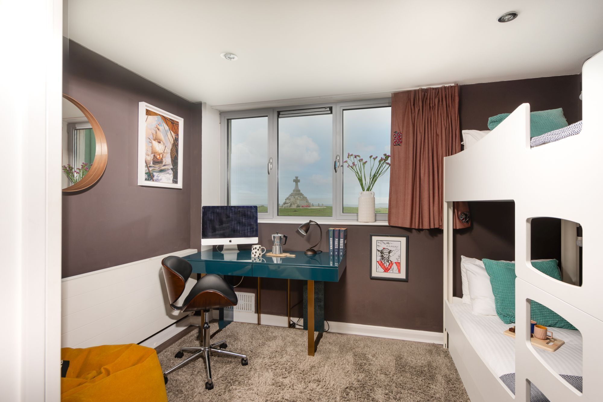 A bedroom with a bunk bed, a desk with a computer, a chair, and a window with a view of a landscape.