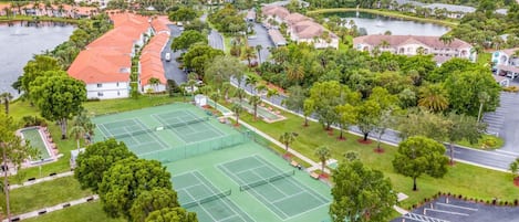 A tennis court surrounded by lush greenery and residential buildings.