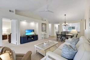 A living room with a television, a dining area, and a ceiling fan. - Sapphire Lakes Topaz (Naples)