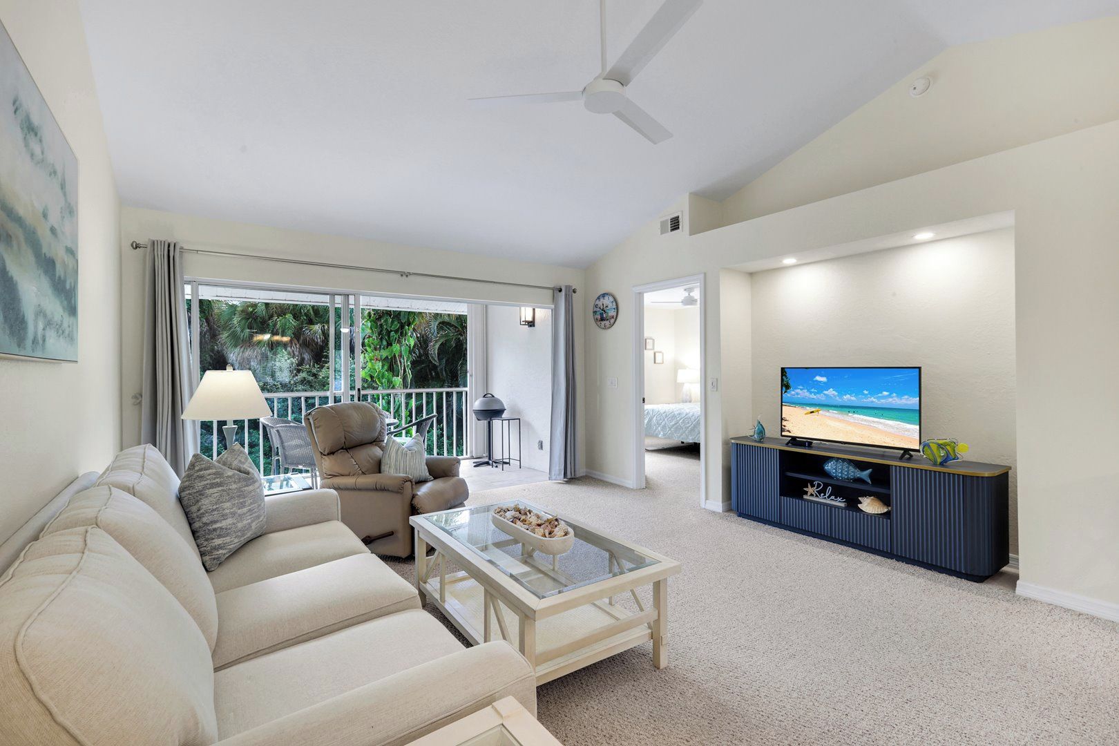 A living room with a sofa, a television, and a balcony with a view of the outdoors.
