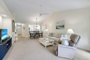 A spacious living room with a television, a dining area with chairs, a sofa, and a coffee table. - Sapphire Lakes Topaz (Naples)