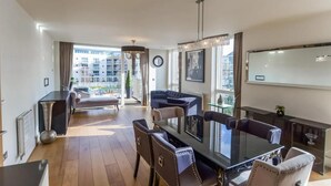 Un salon moderne avec une table à manger en verre, des fauteuils en cuir, un canapé et une vue sur un quartier résidentiel grâce à de grandes fenêtres.